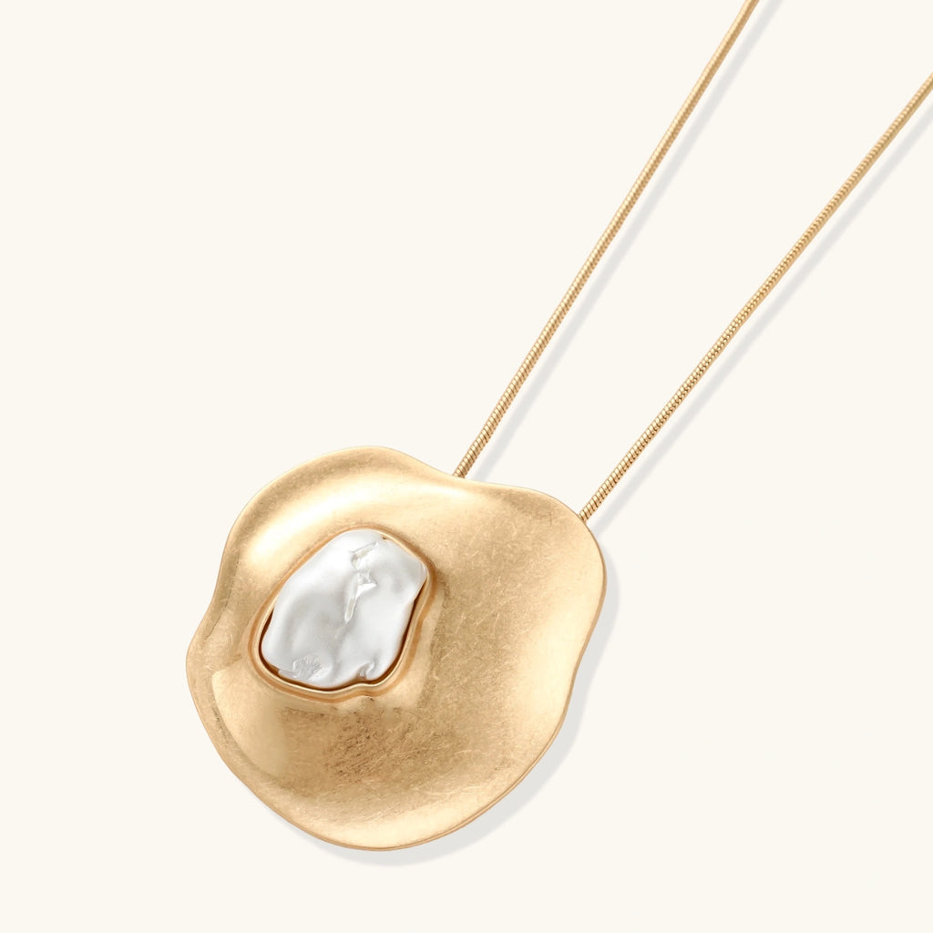 Close-up of organic gold-toned earrings and necklace with white baroque pearls on neutral background.