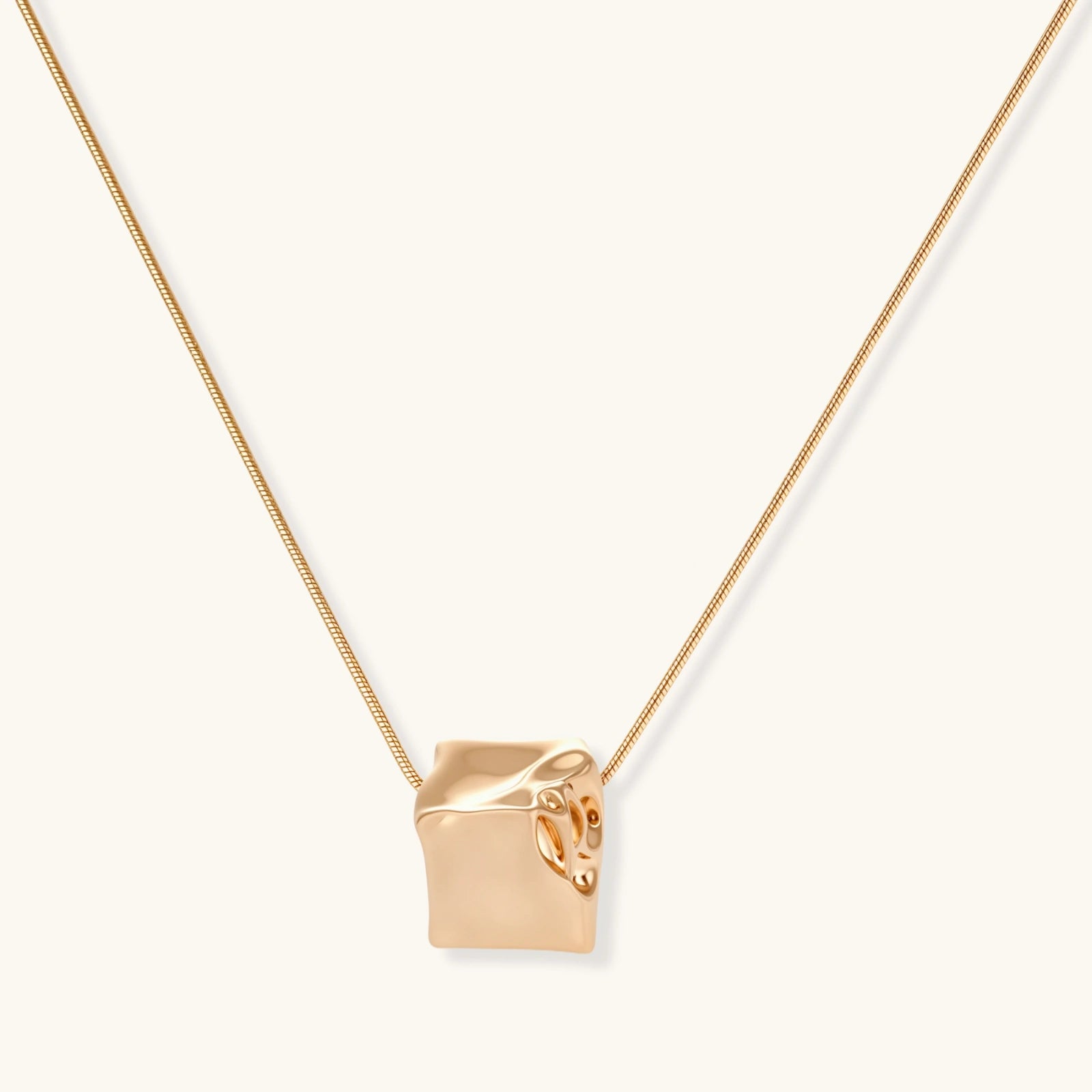 Modern geometric jewelry set featuring crumpled cube pendants in warm gold finish with chain details on beige background.