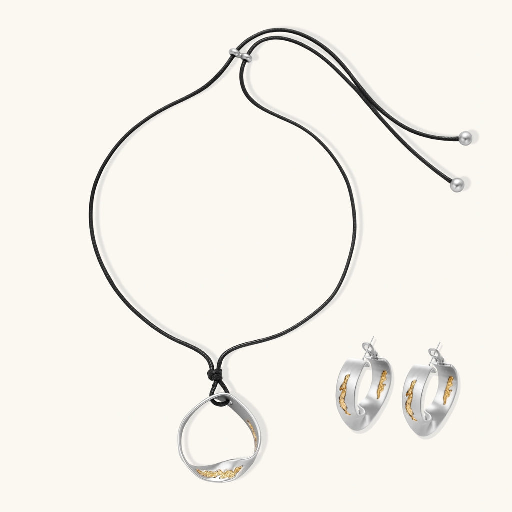 Artistic jewelry set featuring curved silver pendant with gold veining on black cord plus matching asymmetrical hoop earrings